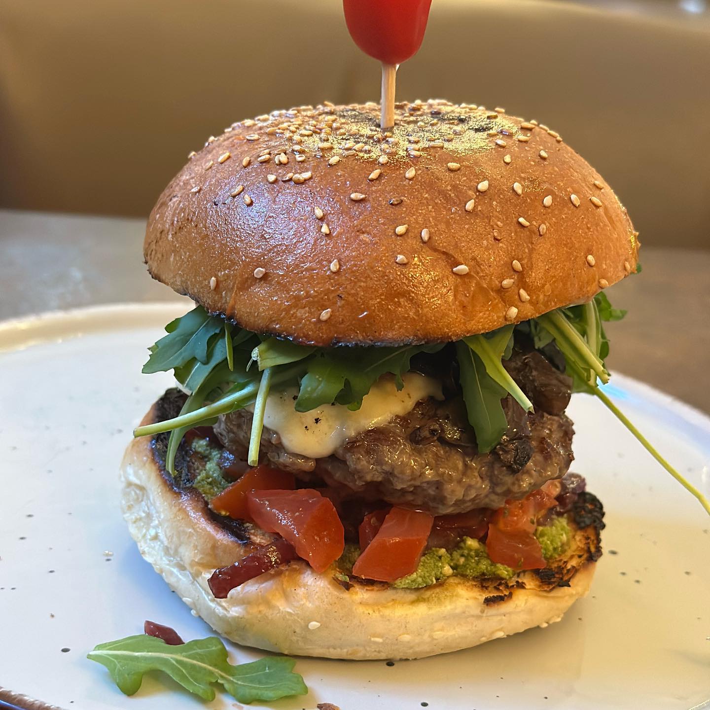 Ein saftiger Burger mit Rucola, Tomaten und Pesto bei moritz Burger 'n Steaks appetitlich auf einem Teller serviert.