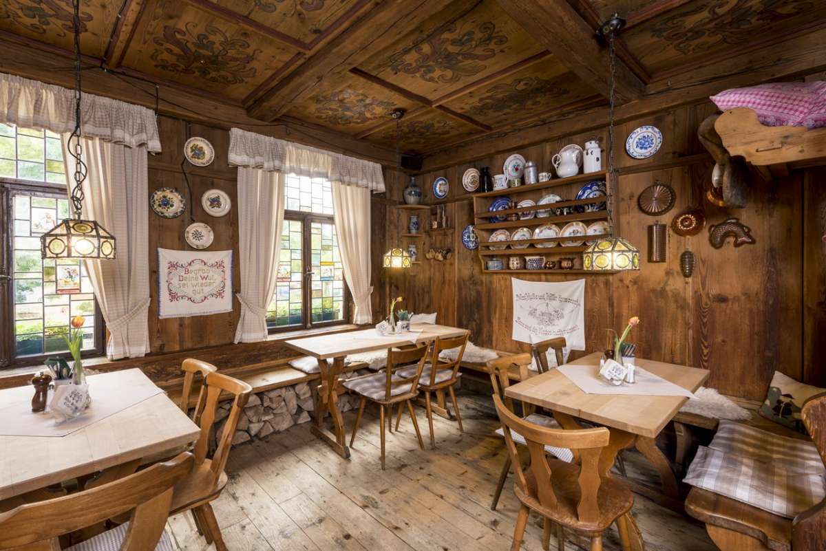 Eine der Stuben des Alten Simpl: bemalte Kassettendecke, Butzenscheiben, Wandregale mit blau-weißem Geschirr und Holzbänke mit gestapeltem Scheitholz darunter.
